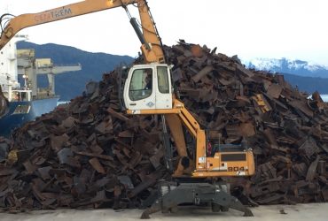 Material handler next to a pile of scrap ferrous metals before loading onto a barge