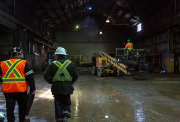 Vue d'un des secteurs du centre de recyclage Centrem à Alma, avec deux employés marchant (vue de dos) et un employé manœuvrant un équipement mobile.
