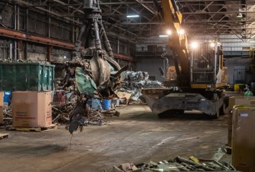 Employee operating material handler equiped with a grapple and moving various waste material at Centrem recycling center in Alma